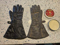 Load image into Gallery viewer, A pair of leather motorcycle gloves laying flat on a table with an open can of Leather better next to the untreated glove on the right. Left leather glove is treated with Leather better.
