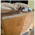 Load image into Gallery viewer, Backside of a tan chair that has the left side of the chair treated with leather better, and the right side untreated to display the results. An open can of leather better is on top of the chair.