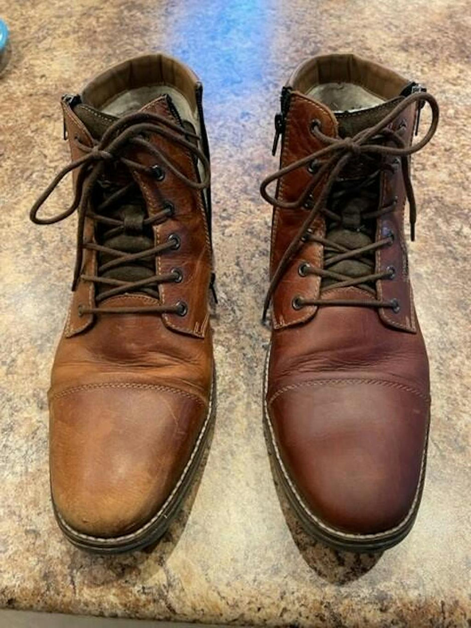 Side-by-side view of a pair of brown leather lace-up boots on a countertop, showing a dramatic before-and-after leather restoration. The right boot appears dry, scuffed, and faded, while the left boot has been fully conditioned, revealing a rich, even tone and smooth finish.