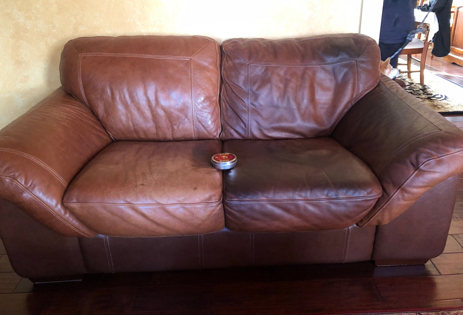 A dark brown leather loveseat with a can of Leather better sitting in the center of the couch. The left side of the couch hasn't been treated and is faded and scratched. The right side of the couch has been treated and restored.