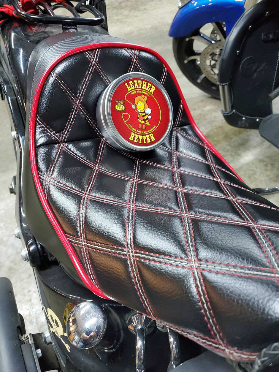 A motorcycle seat with a criss-cross diamond pattern with shiny black leather after being treated Leather better. A tin of Leather better is placed on the seat.