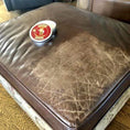 Load image into Gallery viewer, An ottoman that has been treated with Leather Better, but a patch left untreated.  The treated area is a deep chocolate brown and has a tin of Leather Better sitting on it, whereas the untreated patch lis heavily cracked and worn/faded. The difference is striking!