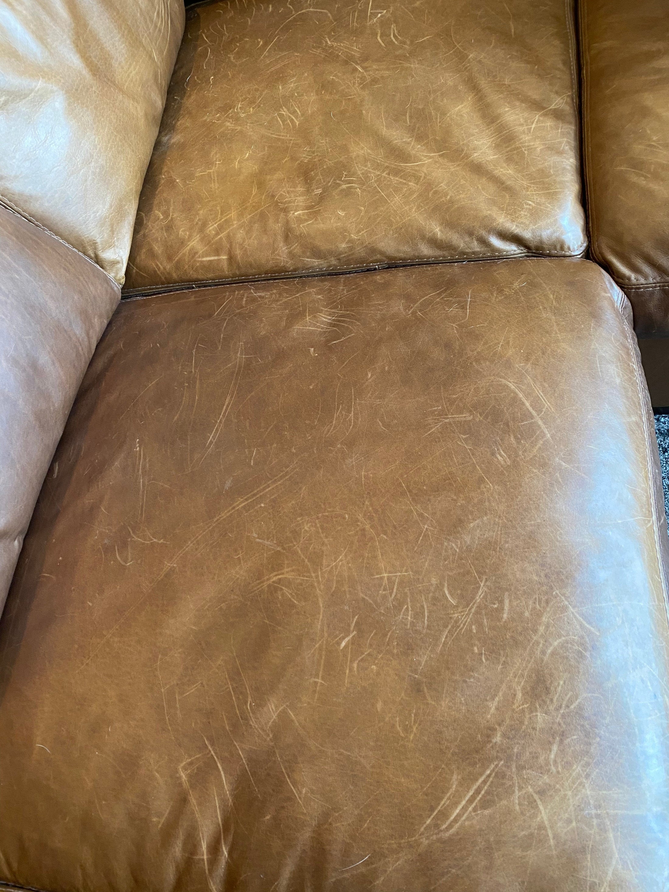 A close up of the seat section on a leather couch showing numerous scratches from a dog, prior to being treated with Leather Better.